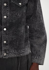 Jachetă din denim negru, cu un model texturat, încheiată cu nasturi metalici argintii și cusături contrastante albe pe margini și tiv.