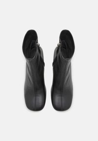 Paire de bottines en cuir noir avec fermetures éclair latérales, bouts carrés arrondis et coutures verticales visibles à l'avant.
