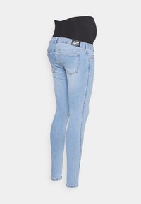 Jeans de maternidade com uma cintura em elástico preta, tecido de denim azul claro, ajuste slim, design de cinco bolsos e leve desvanecimento nos joelhos.