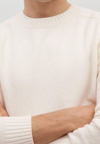 Jasnobeżowy sweter z dzianiny z prążkowanym okrągłym dekoltem i ściągaczami na mankietach. Miękka faktura, długie rękawy oraz luźny krój. Brak widocznych wzorów lub logo.