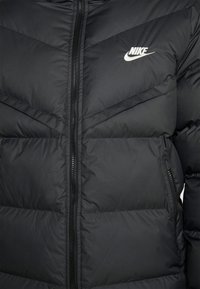 Black puffer jacket featuring a zip closure, horizontal quilted design, and a small white Nike logo on the upper left side.