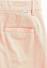 Levi's ljusrosa byxor har en bakficka med en sydd kant, en märkestagg och en slät bomullsblandning.