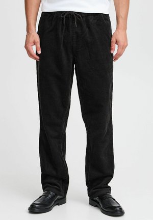 Black corduroy pants with a relaxed fit, featuring vertical ribbing, an adjustable drawstring waist, and sleek black shoes.