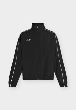 Jachetă neagră cu fermoar și guler înalt, cu tivuri albe de-a lungul mânecilor, manșete și tiv elastic și logo ARKK pe pieptul stâng.