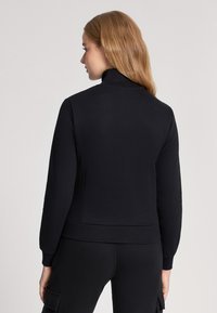 Felpa nera con zip, colletto alto, design aderente, polsini e orlo a costine. Realizzata in un tessuto morbido con una texture liscia.