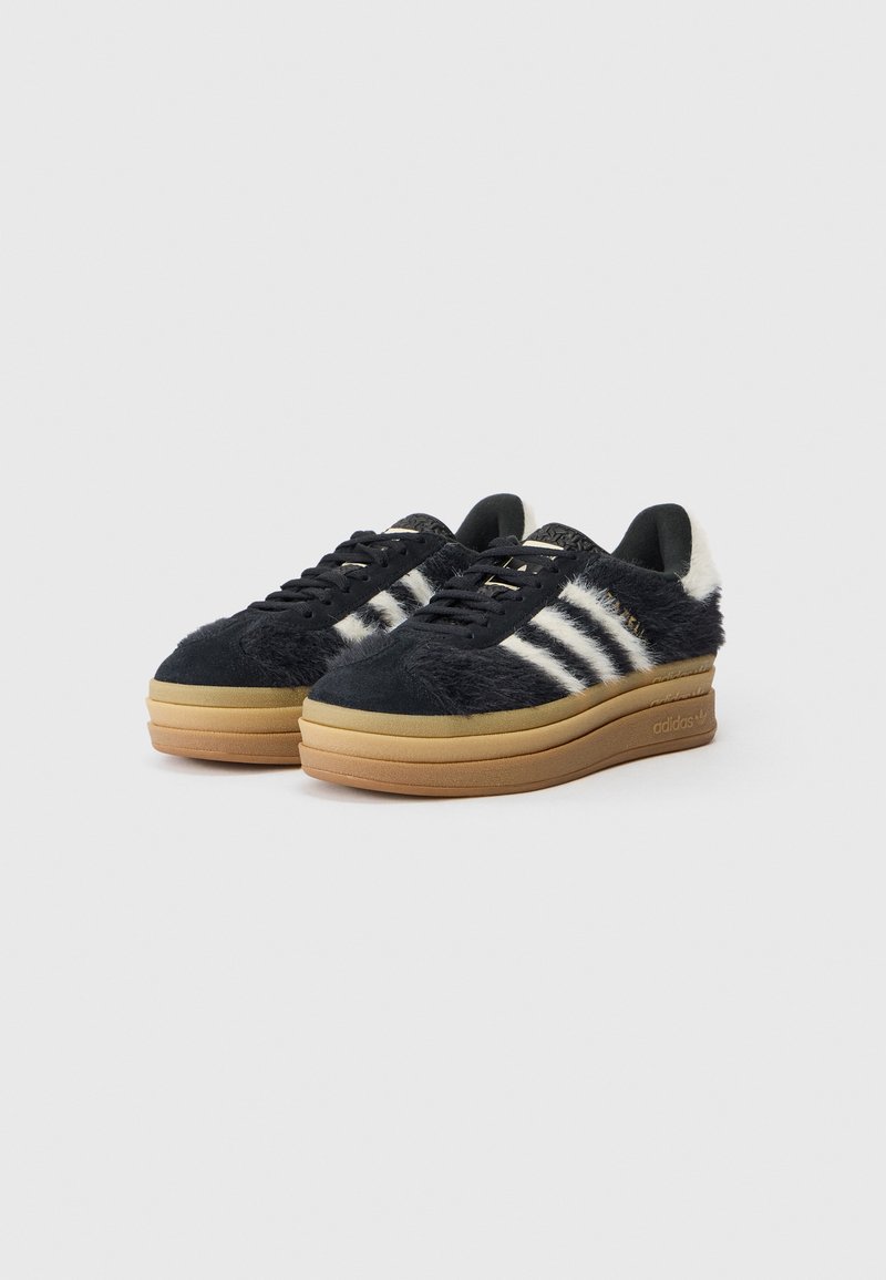 Schwarze und weiße, fellmusterte Sneakers mit einer beigen Plateausohle. Verfügt über runde Schnürsenkel und drei weiße Streifen an den Seiten.