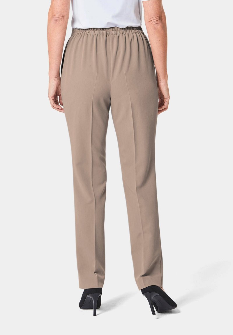 Beige, elastische taillebroek met een rechte pasvorm en een voorplooidetail, gecombineerd met zwarte hoge hakken, gezien van achteren.
