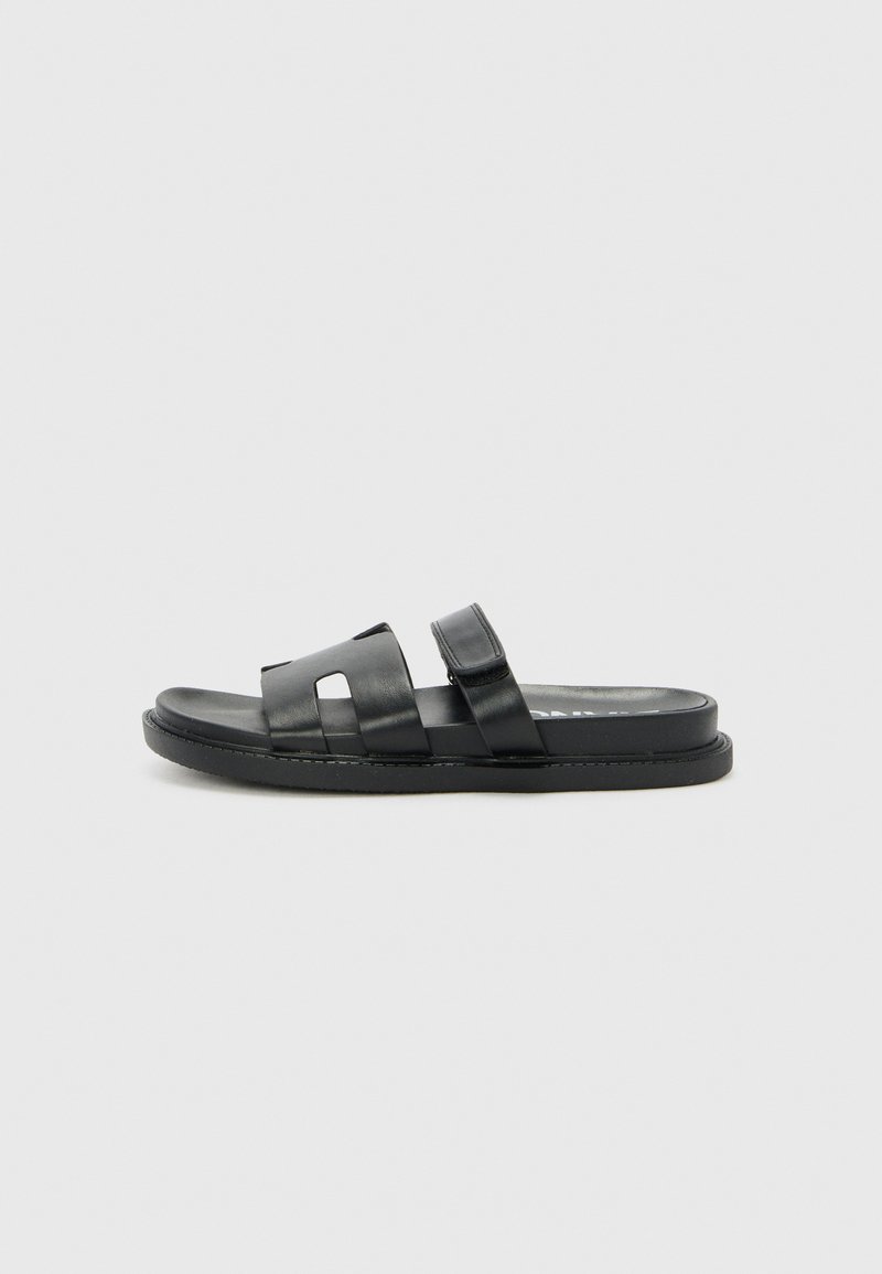 Sandalhas de slide em couro preto com duas tiras largas, design de ponta aberta e sola plana. Estilo minimalista com detalhes cosidos na sola.