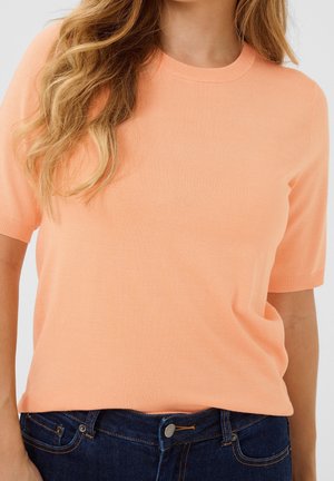 Trui met korte mouwen en ronde hals, gemaakt van zachte perzikkleurige breiwerk. Heeft een aangesloten model met geribbelde manchetten en een rechte zoom. Gecombineerd met donkerblauwe jeans.