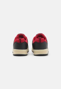 Baskets de sport noires et rouges avec tige en mesh, semelle en caoutchouc et col rembourré. Présente des accents contrastés et une finition texturée.