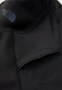 Svart langermet topp laget av glatt, elastisk materiale med flate sømmer. Har en logo på kragen og et minimalistisk design.