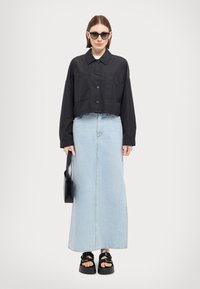 Cămașă neagră scurtă cu butoane, prevăzută cu două buzunare în față, asortată cu o fustă maxi din denim albastru deschis, sandale negre cu platformă și o geantă de umăr neagră.