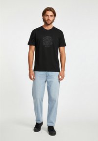 Černé bavlněné tričko s potiskem lva v tmavě šedé barvě, spárované se světle modrými džíny rovného střihu a černými teniskami.