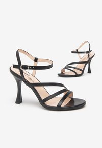 Sandalias de tacón alto negras con tiras finas, acabado en cuero suave, correa de tobillo asegurada y diseño de tacón acampanado.