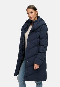 Tumši zila pūkainā mēteli ar cepuri, ar spiedpogu aizdari un izšuvumu. Valkāta virs viegla krekla un saskaņota ar džinsiem.