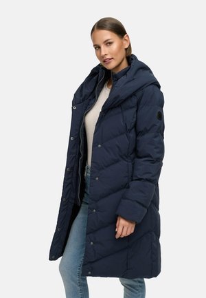 Navy blue puffer coat with a hood, featuring snap buttons and quilted texture. Worn over a light top and paired with jeans.