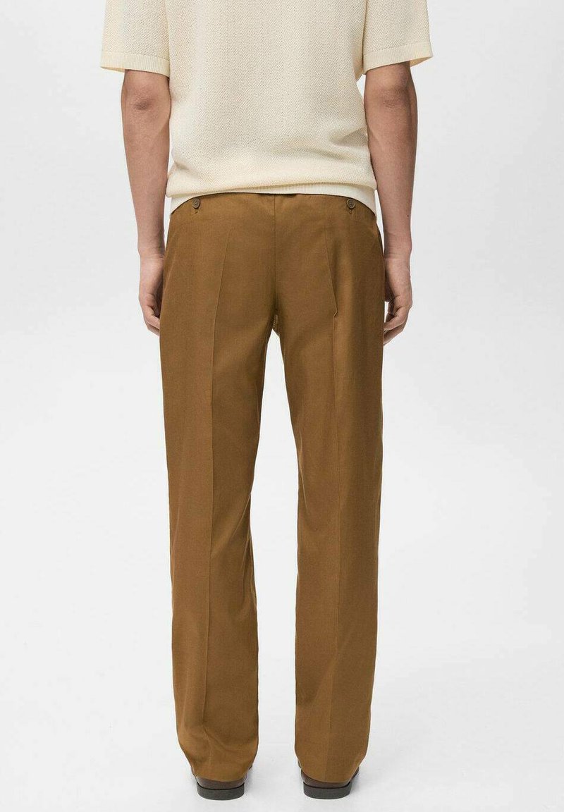 Pantaloni marroni a gamba dritta in tessuto liscio, con due tasche posteriori e pieghe come dettaglio di design. Indossati con un top chiaro.