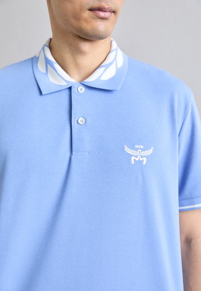Ljust blå polo t-shirt med en vit mönstrad krage och vit broderad logotyp på vänster bröst. Klassisk passform med knäppning.