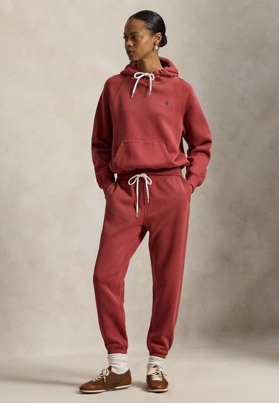 Rød bomullshettegenser med snor og frontlomme, kombinert med matchende joggebukser med elastiske mansjetter og linning. Brune sko med hvite sokker.