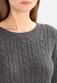 Grå stickad tröja med ett kabelmönster, ribbads halsringning och mjuk textur, som framhäver vertikala linjer i tygdesignen.