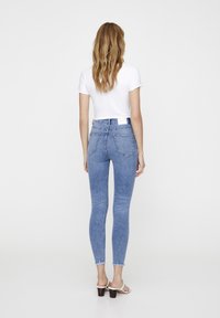 Un jean skinny bleu taille haute, avec un ourlet effiloché et des poches arrière traditionnelles. Associé à une chemise blanche ajustée à manches courtes.