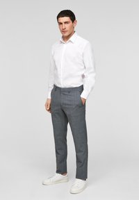 Witte lange mouwen overhemd met een knoopsluiting, gecombineerd met grijs geruite broeken. De broeken hebben zijzakken en een getailleerde pasvorm, aangevuld met witte sneakers.