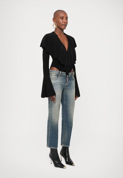 Μαύρο κορμάκι με βολάν στο μπροστινό μέρος, μακριά μανίκια καμπάνα, συνδυασμένο με ξεβαμμένο μπλε τζιν κανονικής γραμμής και μαύρα μποτάκια αστραγάλου με χρυσές λεπτομέρειες.