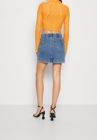 Virkat orange långärmad topp som kombineras med en ljusblå denim minikjol med bakfickor. Svarta sandaletter med rund klack.