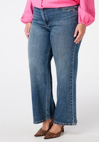 Blauwe, wijde jeans van denimstof met een vervaagde was, gestikte details en een rechte zoom, gecombineerd met puntige hakken in luipaardprint.