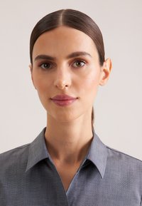 Camicia grigia con bottoni e colletto, caratterizzata da una texture sottile e un design aderente. Il tessuto sembra morbido e leggero.