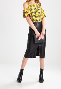 Gul mønstret off-shoulder bluse parret med en sort læder nederdel til knæene, der har en slids foran. Sorte ankla støvler og clutch taske.