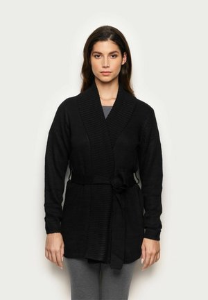 Schwarze Strickjacke mit Schalkragen, strukturiertem Stoff und Gürtel. Verfügt über lange Ärmel und eine lockere Passform. Trägt man über grauen Hosen.