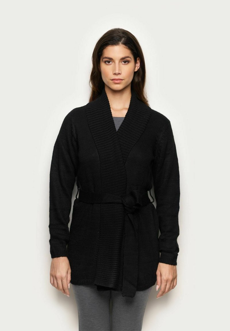 Czarny sweter z dzianiny z kołnierzem typu szal, teksturowany materiał i pasek. Posiada długie rękawy i luźny krój. Nosi się go na szare spodnie.