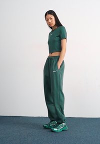 Roheline lühikeste varrukatega T-särk ja sellele sobivad joggersid pehmest kangast, Nike logo aktsentidega. Jalatsid sisaldavad läikivaid rohelisi elemente ja tekstuurset disaini.