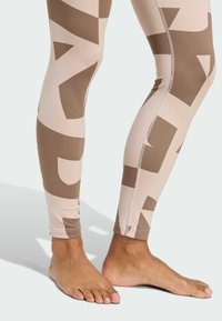 Leggings beige con un gran patrón geométrico abstracto en marrón, con textura suave y diseño ajustado, que terminan justo por encima del tobillo.