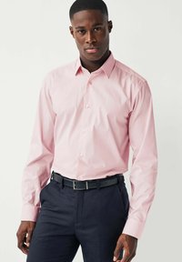 Hellrosa langärmliges Hemd mit button-down Kragen und geradem Schnitt, kombiniert mit dunklen Hosen und einem schwarzen Gürtel.