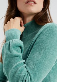 Texturerad, teal färgad turtleneck-tröja med ribbade manschetter och avslappnad passform. Tyget verkar mjukt och mysigt, lämpligt för svalt väder.