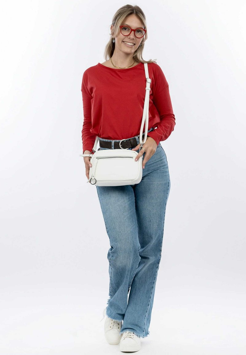 Borsa a tracolla bianca con tasca con zip, texture in pelle liscia. Top rosso a maniche lunghe, jeans a palazzo blu, sneakers bianche. Sfondo in luce naturale.