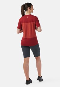 Short-sleeve red top with a textured upper section, paired with dark gray shorts and black footwear. Simple design with minimal accents.