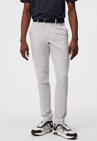 Světle šedé slim-fit kalhoty vyrobené z hladké tkaniny, s klasickým designem, černým tkaným páskem a bílými sportovními botami.