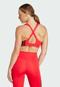 Rode sport-bh met kruislings banden, zwarte accenten en een verstelbare haak. Gecombineerd met hoge rode legging met zwarte zijstrepen.