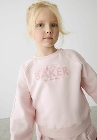 Gaiši rozā sporta krekls ar raglanu piedurknēm, apdrukāts ar "Baker by Ted" logo tumšāk rozā krāsā. Gluda auduma tekstūra un ribotas piedurknes apakšā.
