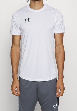 Mandetorso iført en hvid Under Armour kortærmet T-shirt og grå Under Armour shorts mod en ensfarvet baggrund.
