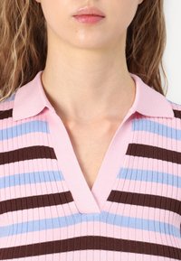 Πλεκτό πόλο μπλουζάκι με κατακόρυφες ρίγες σε ροζ, μπλε και καφέ. Διαθέτει V-λαιμόκοψη και ριμπ υφή με κοντό γιακά.