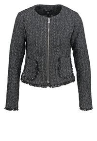 Veste femme texturée noir et blanc avec fermeture éclair devant, col rond, deux poches avant et bords frangés aux manches et à l'ourlet.