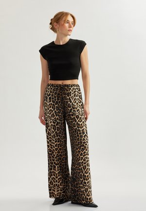 Top nero corto, pantaloni larghi con stampa leopardata e vita con cordino, caratterizzati da una texture setosa e scarpe nere lucide.