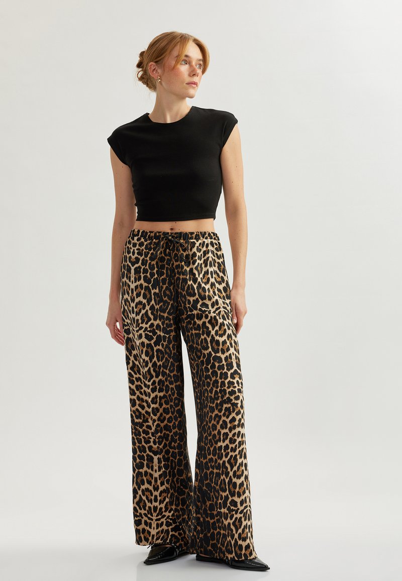 Zwart cropped top, wijde leopardprint broek met een trekkoord in de taille, met een zijdezachte textuur en hoogglanzende zwarte schoenen.
