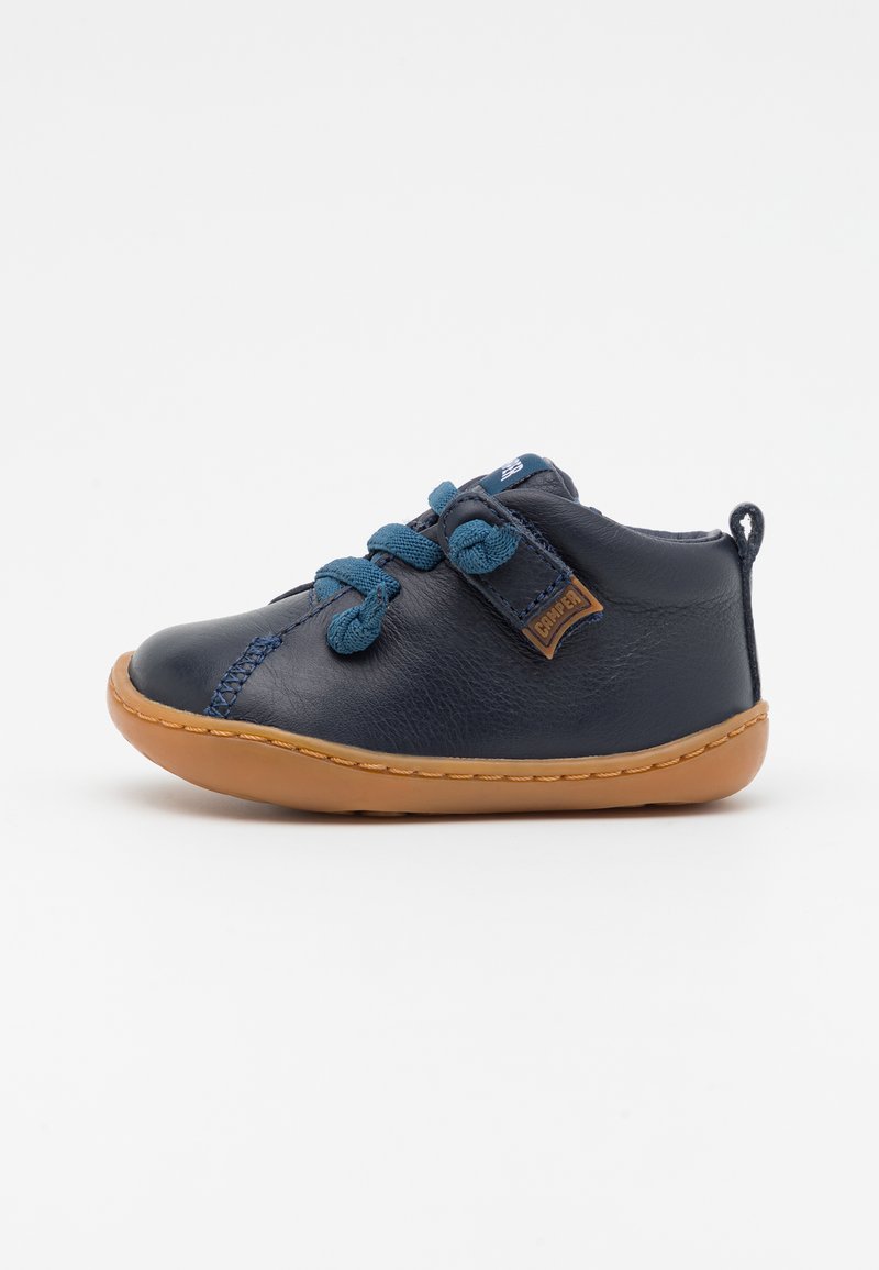 Chaussure en cuir bleu marine à bout rond, finition texturée, lacets bleus et semelle en caoutchouc marron. Présente un petit patch en cuir sur le côté.