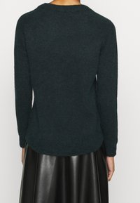Tmavě zelený pletený svetr s kulatým výstřihem a dlouhými rukávy. Materiál působí měkce, s mírně chlupatou texturou a zaobleným lemem.