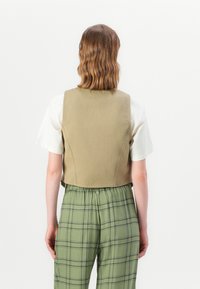 Beige vest laget av bomull med en tettsittende design, kombinert med lysegrønne rutete bukser med elastisk liv og knappdetaljer.